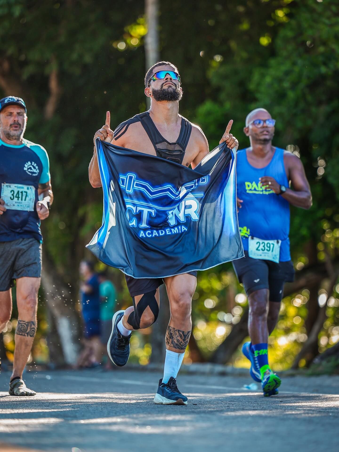 Wanderson Ramos cruzando a linha de chegada de uma corrida de rua, erguendo a camisa com a marca do Centro de Treinamento WR.